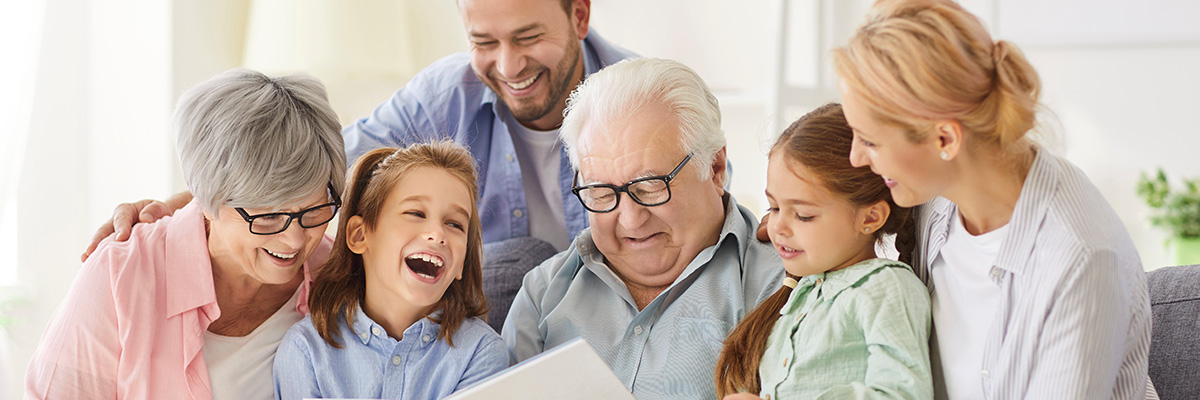 Mehrgenerationenfamilie sitzt zusammen auf einem Sofa und schaut sich eine Zeitschrift an.