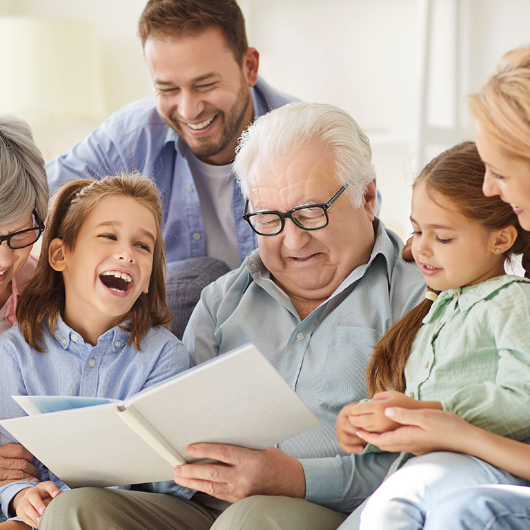 Mehrgenerationenfamilie sitzt zusammen auf einem Sofa und schaut sich eine Zeitschrift an.