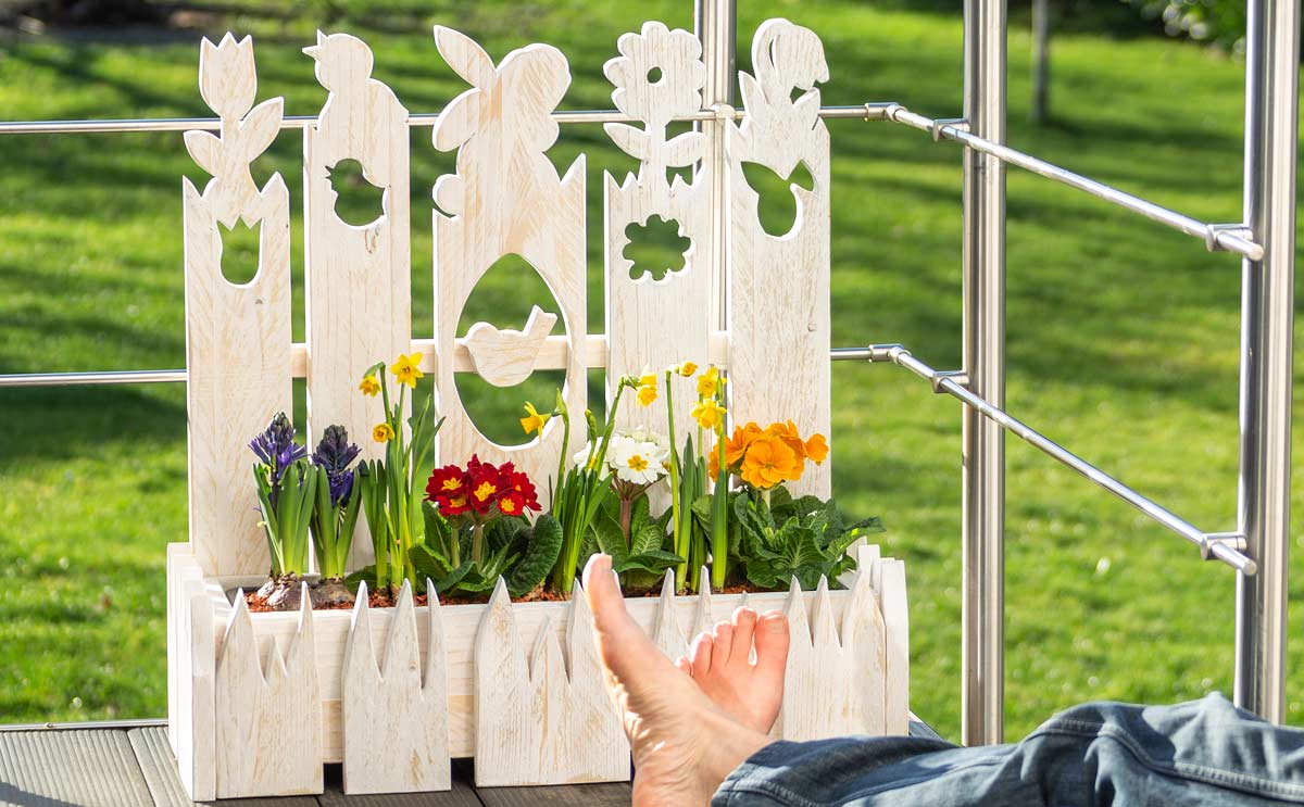 Dekorativer Oster-Pflanzkasten aus Holz mit Fr&uuml;hlingsblumen auf Balkon 